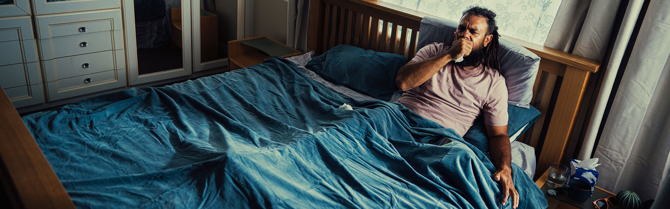 Man with flu laying in bed coughing into a tissue